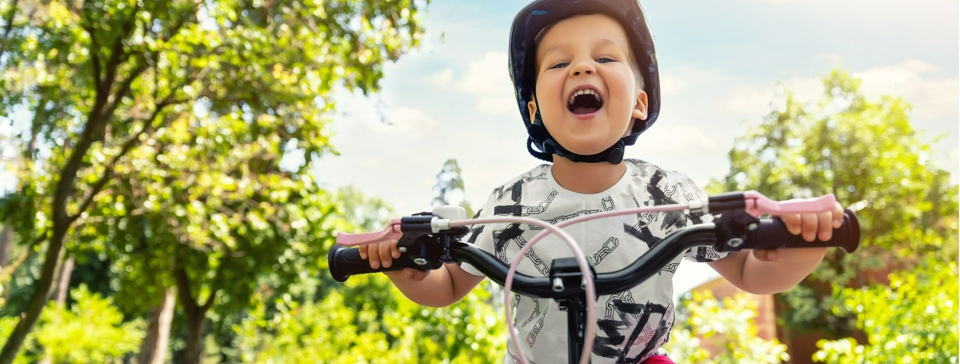 Criança sorrindo andando de bicicleta num dia ensolarado
