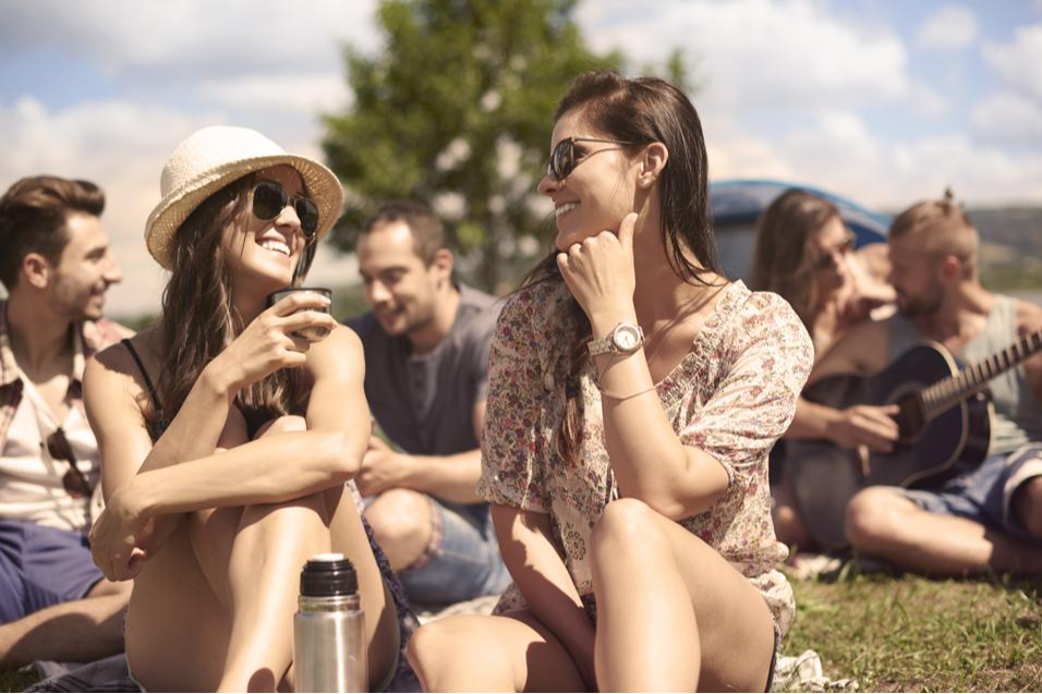 duas amigas olhando uma para outra sentadas em grama em festival